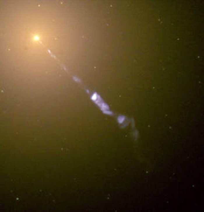 M87星系的中心闪耀着一个巨大的宇宙探照灯：从黑洞向外喷射出的次原子粒子流的速度接近光速。 在这张哈伯太空望远镜所拍摄的影像中，蓝色的喷流与M87星系中恒星和星
